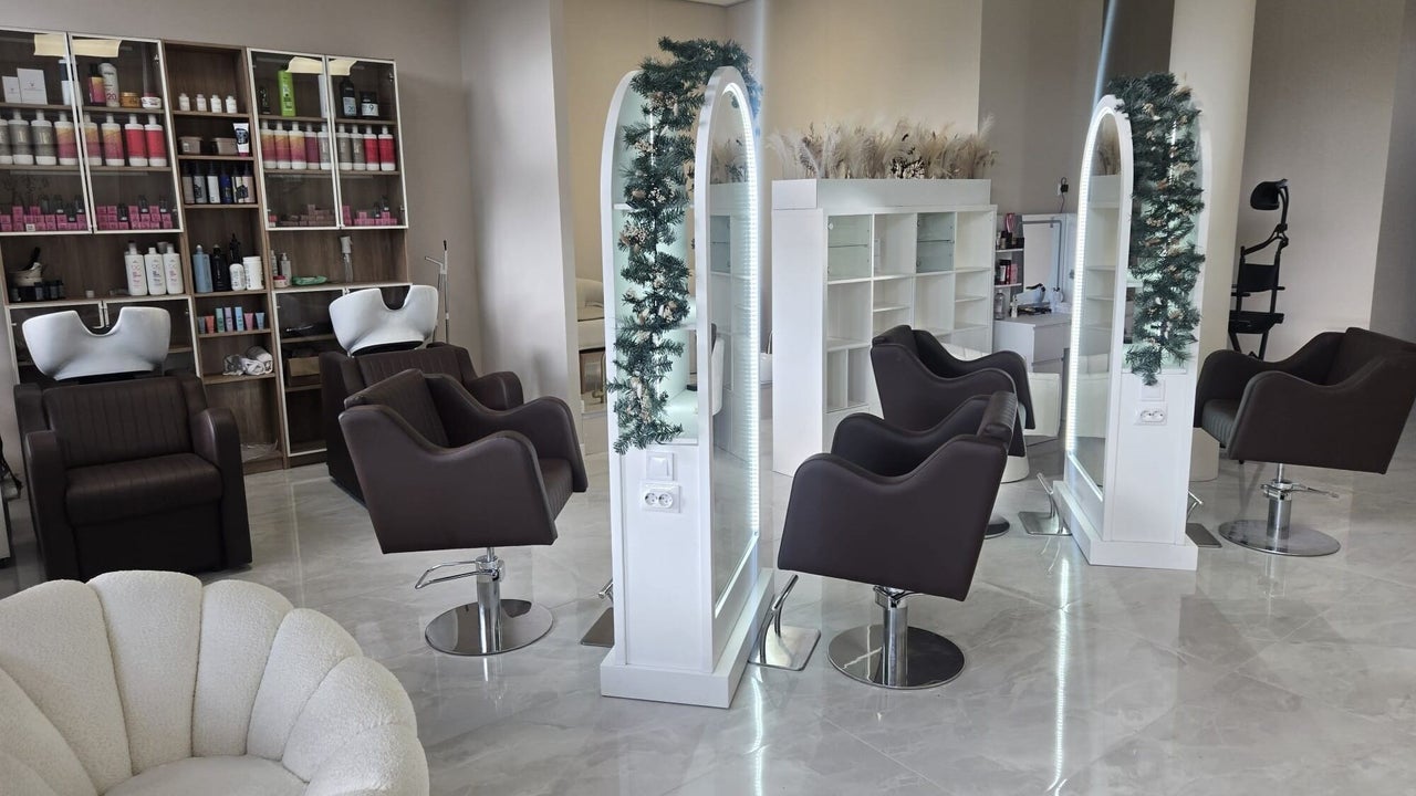 Zwarte kappersstoelen, wasbakken en een gebogen spiegel met groen in de salon